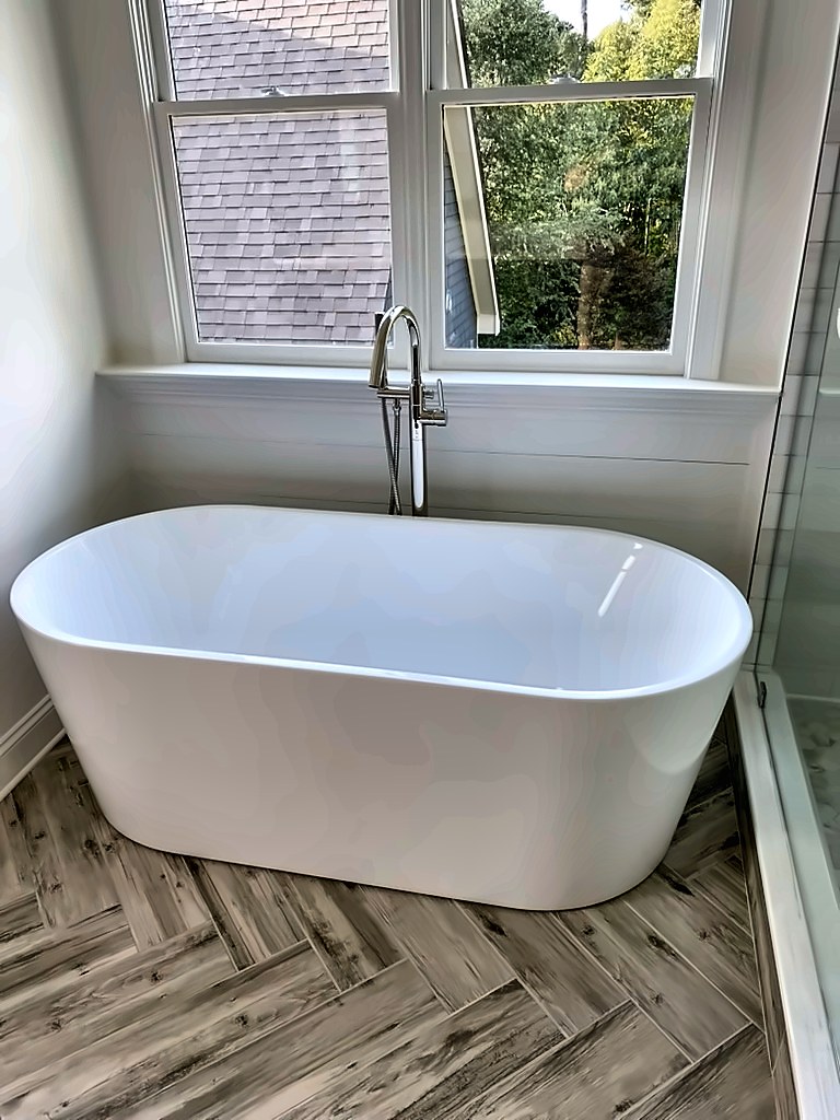 Freestanding soaking tub under a window with herringbone tile floor